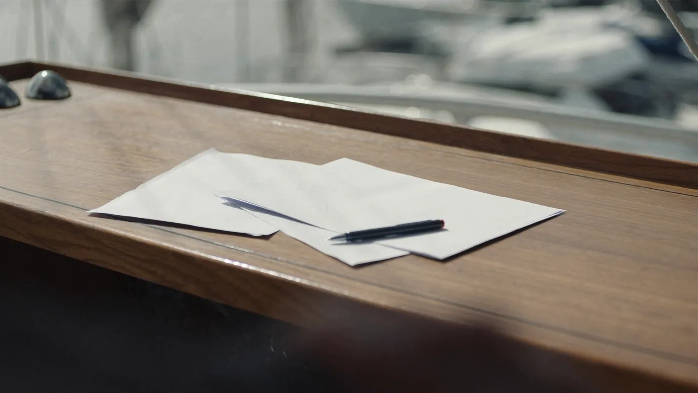 Documenti e penna sul tavolo in teak del pozzetto di una barca, porto sullo sfondo